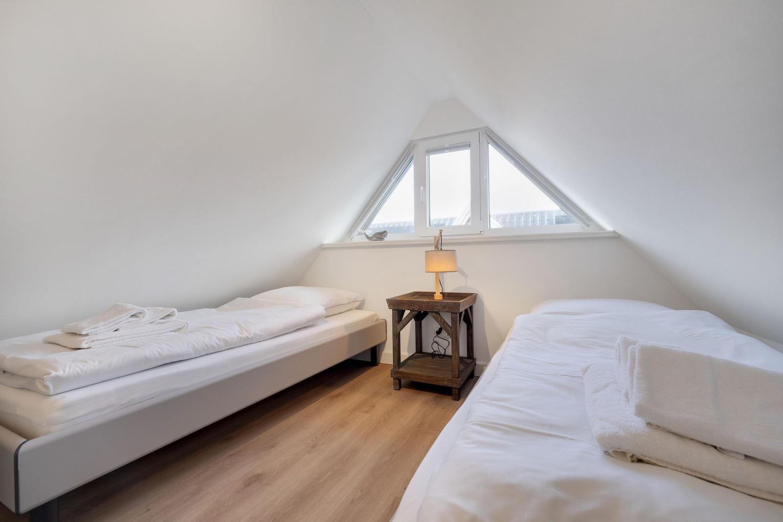 Zwei Betten in einem Dachzimmer mit Dachfenster und Holzboden.