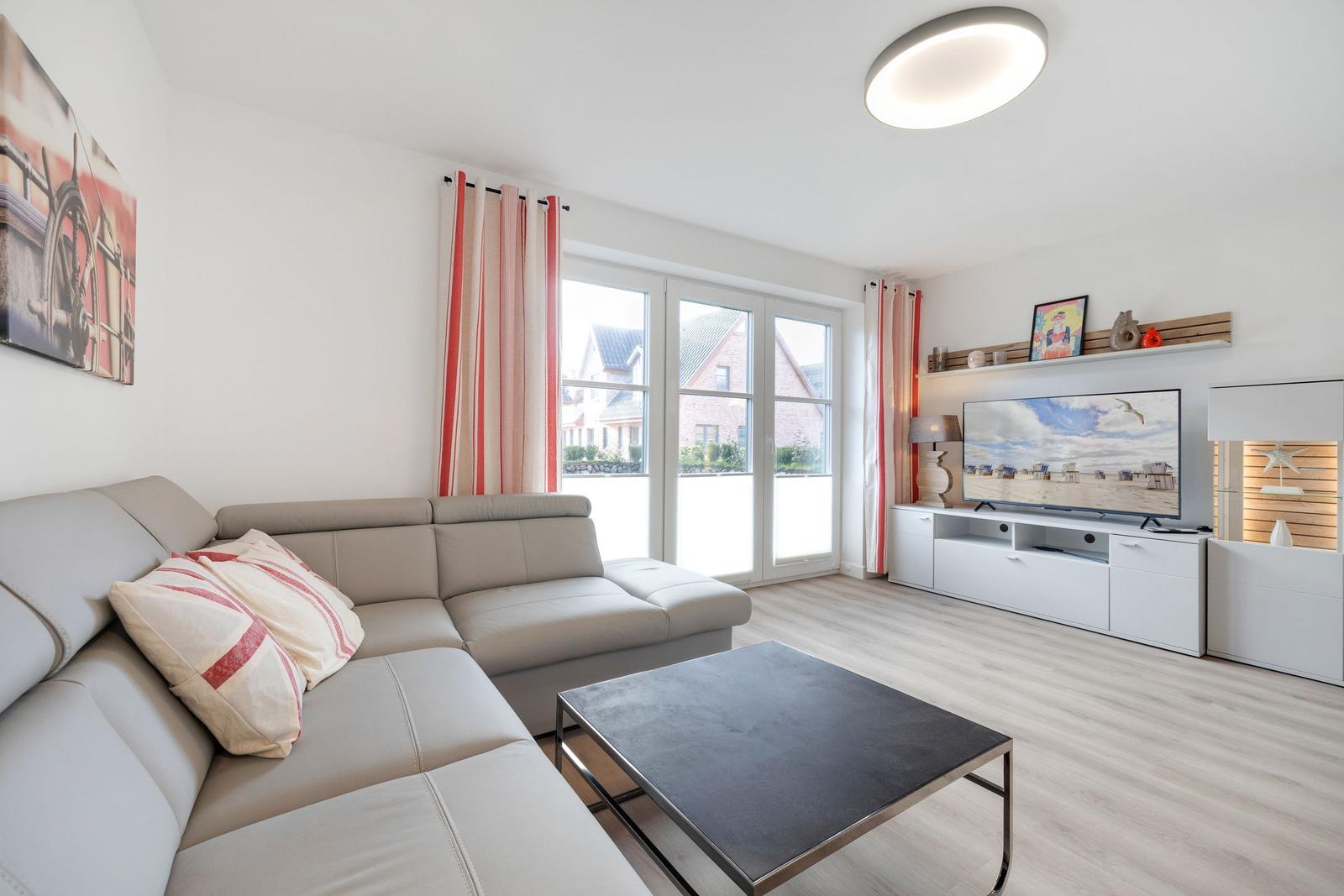 Wohnzimmer mit Sofa, Couchtisch und TV. Fenster mit Vorhängen. Holzboden.
