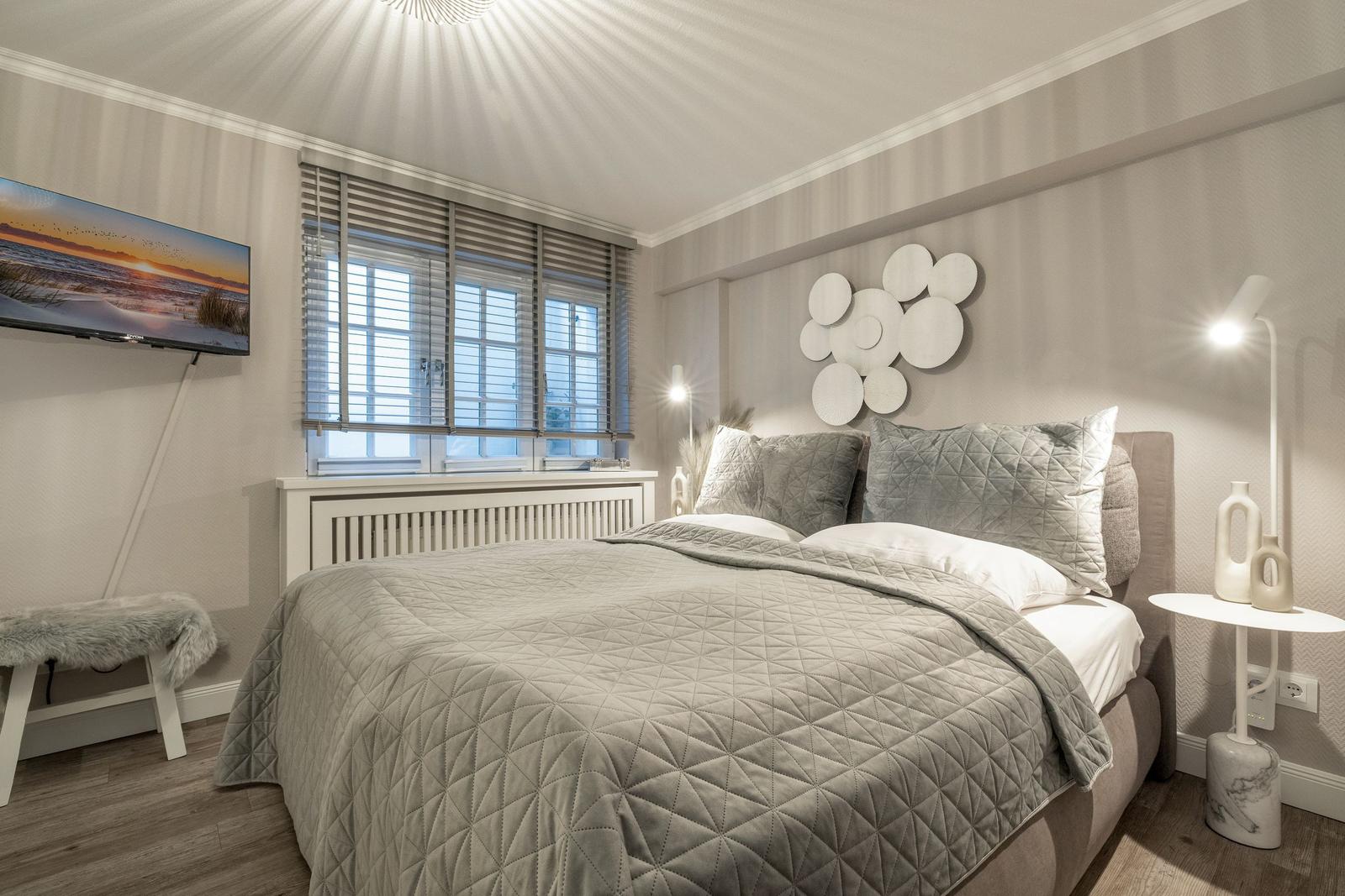 Schlafzimmer mit Bett, Fenster, Wanddekoration und Fernseher an der Wand.