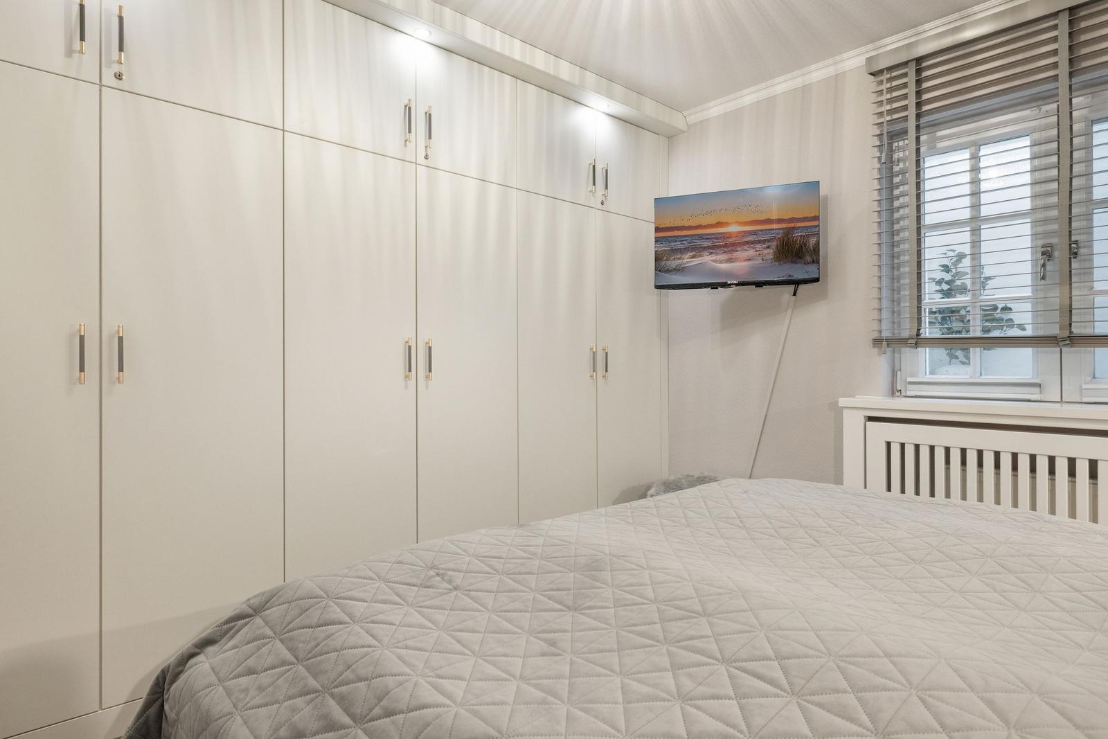Schlafzimmer mit großem Schrank, Bett und Wand-TV.