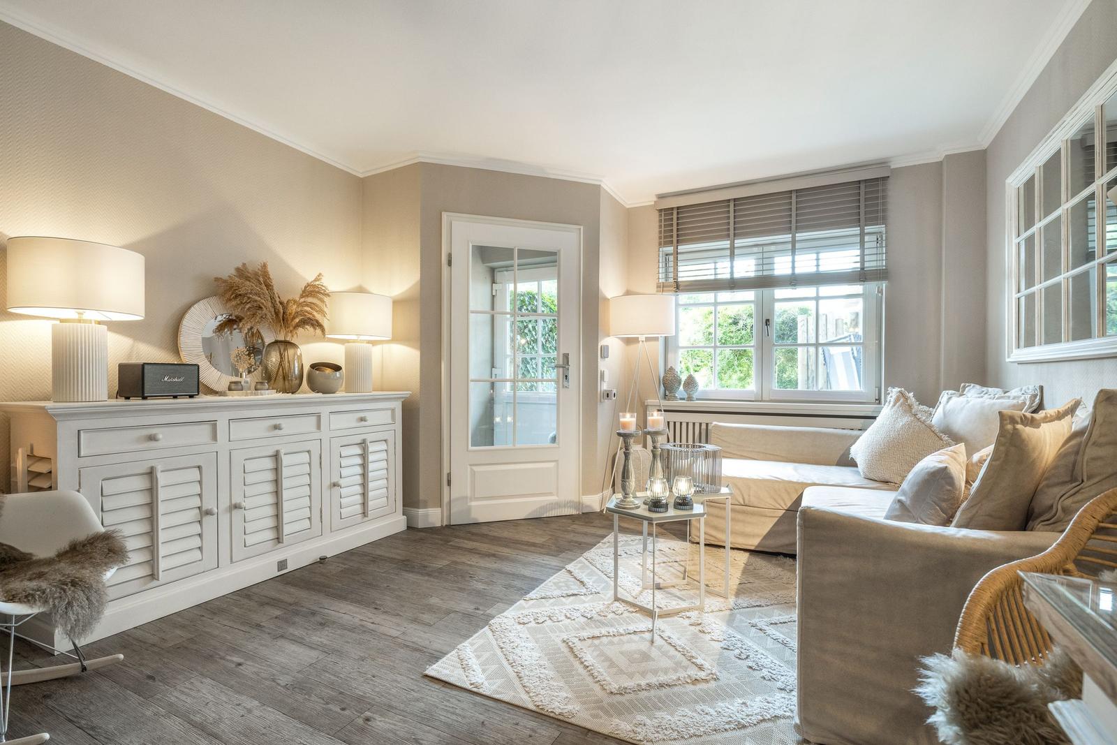 Wohnzimmer mit Sofa, Sideboard und Fenster. Holzboden und Beleuchtung.