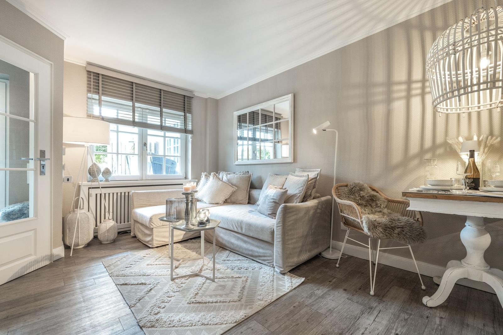 Wohnzimmer mit Sofa, Tisch, Stuhl und Fenster. Wandspiegel und Deckenleuchte sichtbar.