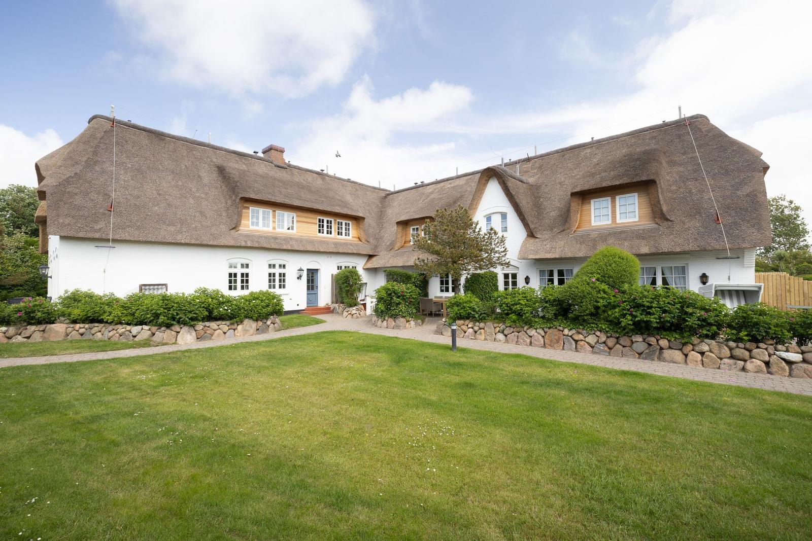 Ein weißes Haus mit strohgedecktem Dach und grünem Garten.