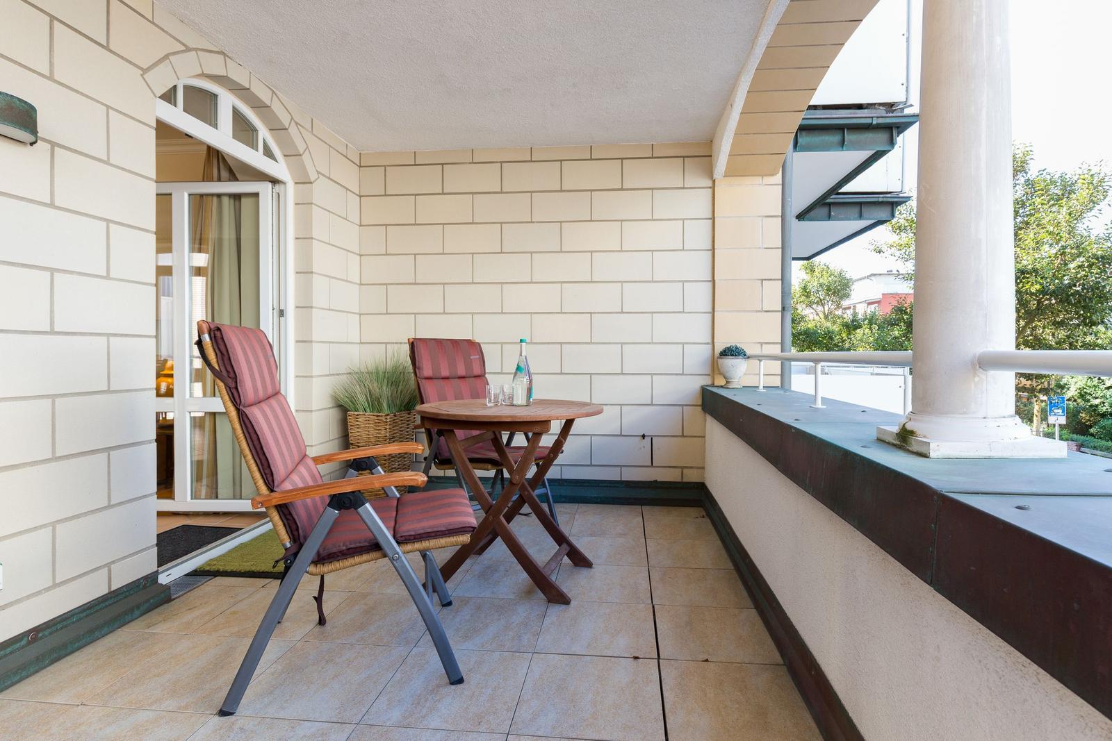 Terrasse mit Tisch, zwei Stühlen und Pflanzen. Durchgang zur Wohnung.