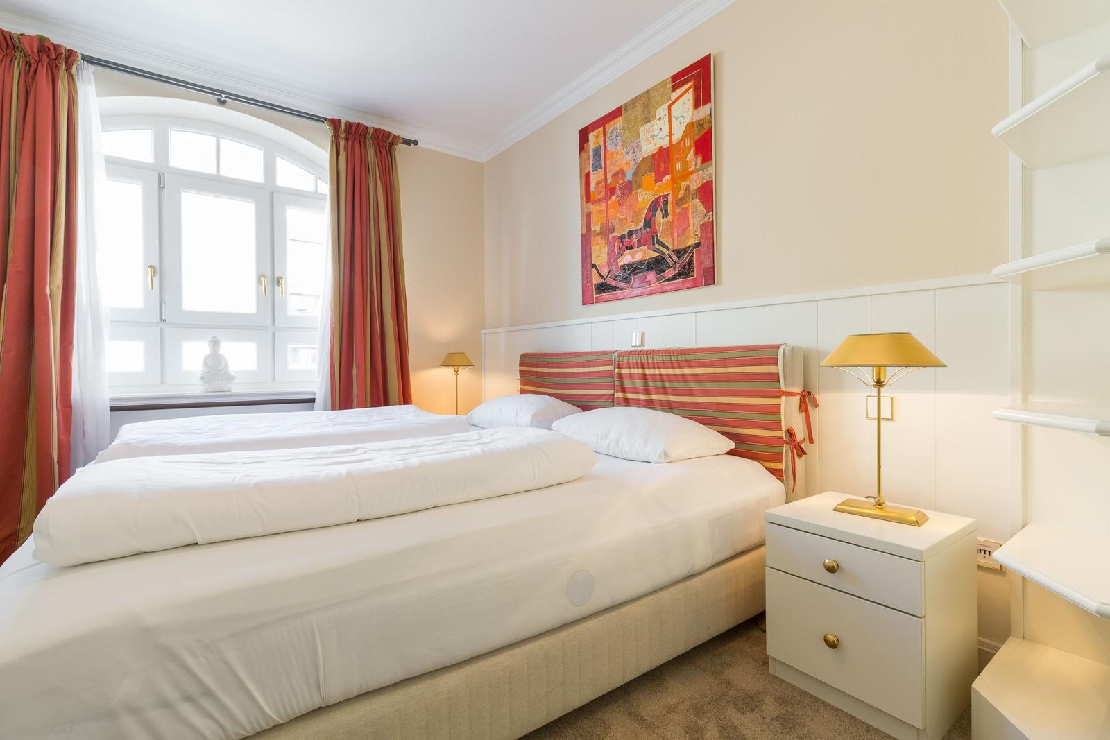 Schlafzimmer mit Doppelbett, Fenster, Gemälde und Nachttisch.