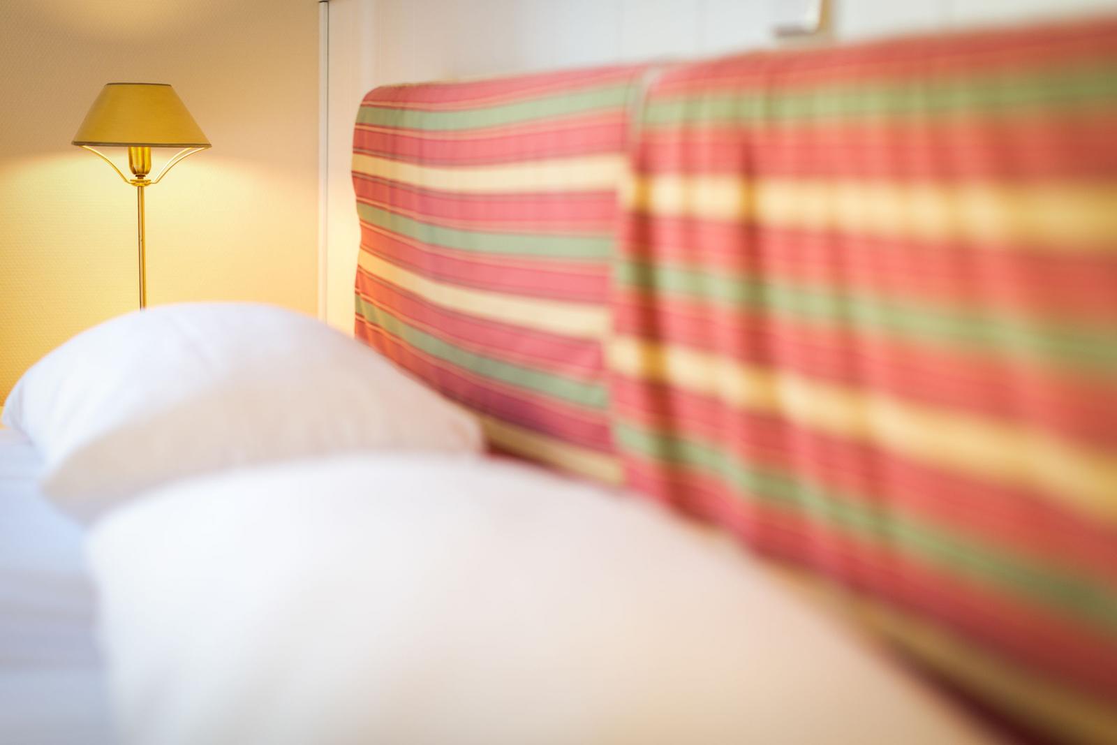 Bettkopf mit gestreifter Abdeckung und Stehlampe im Hintergrund.