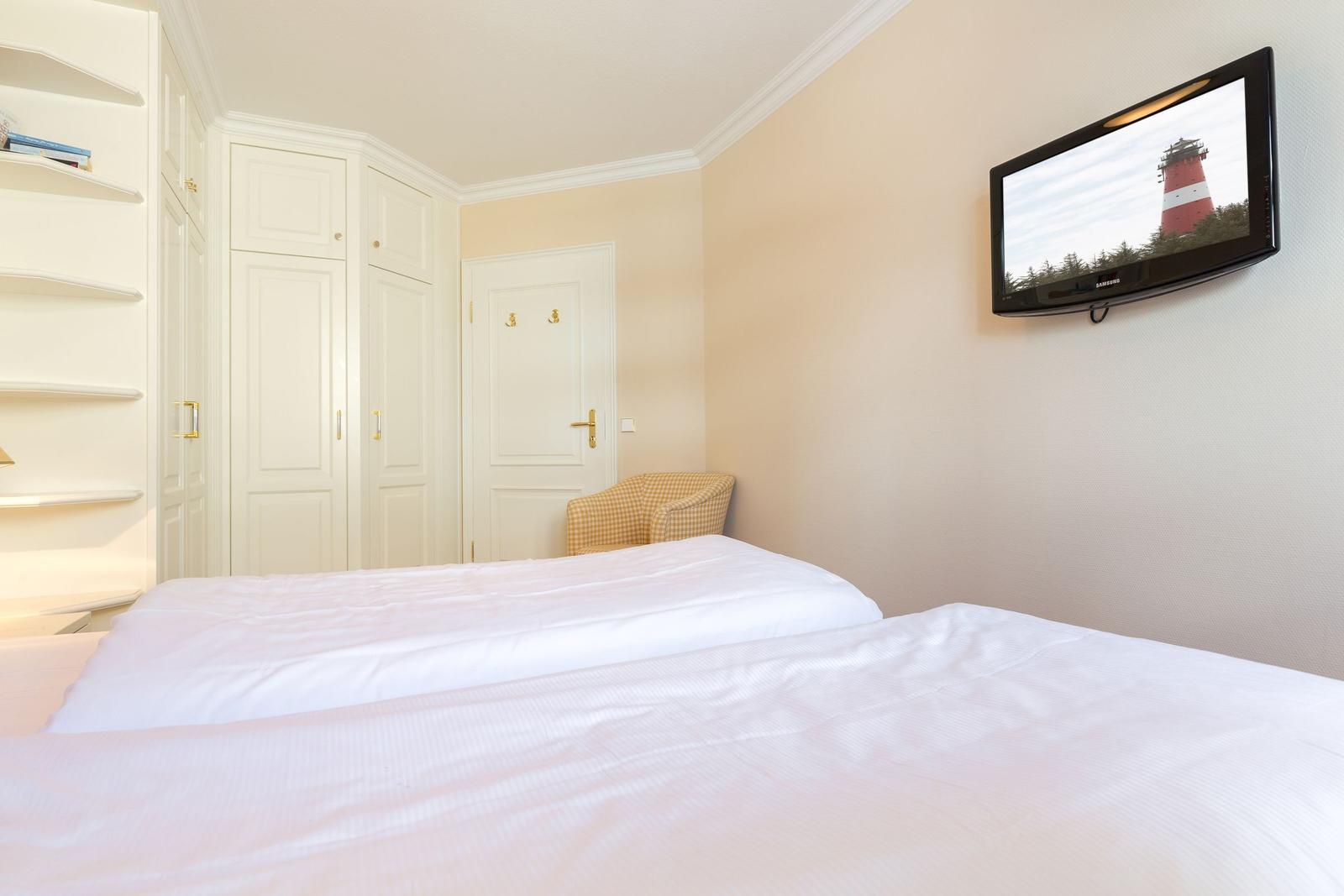 Schlafzimmer mit Bett, Kleiderschrank und Wandfernseher.