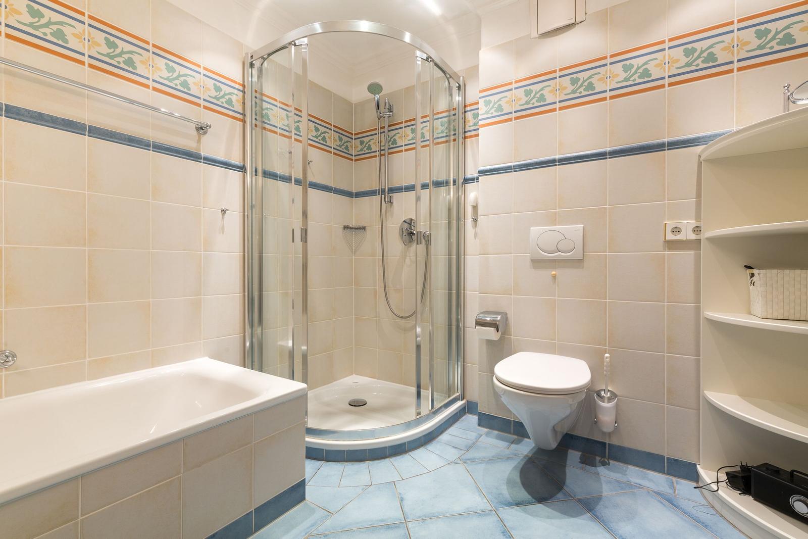 Badezimmer mit Dusche, Badewanne und Toilette. Fliesen mit floraler Bordüre.