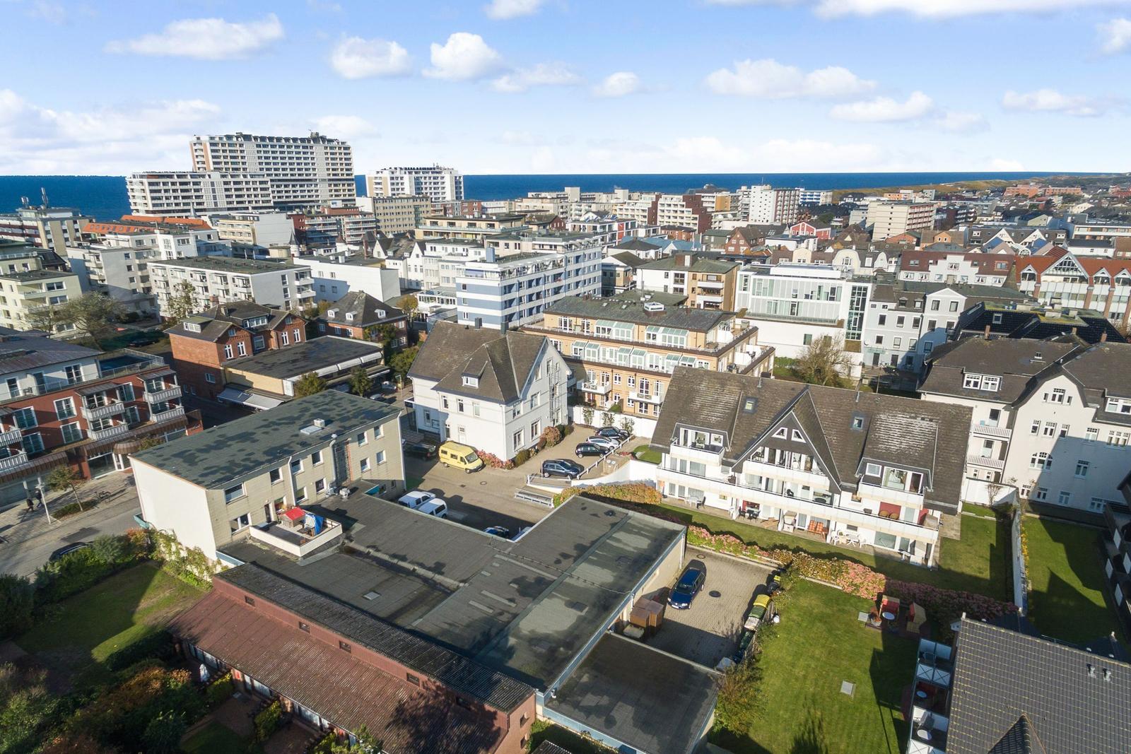 Aerial view of coastal town with houses, gardens, and ocean in background.