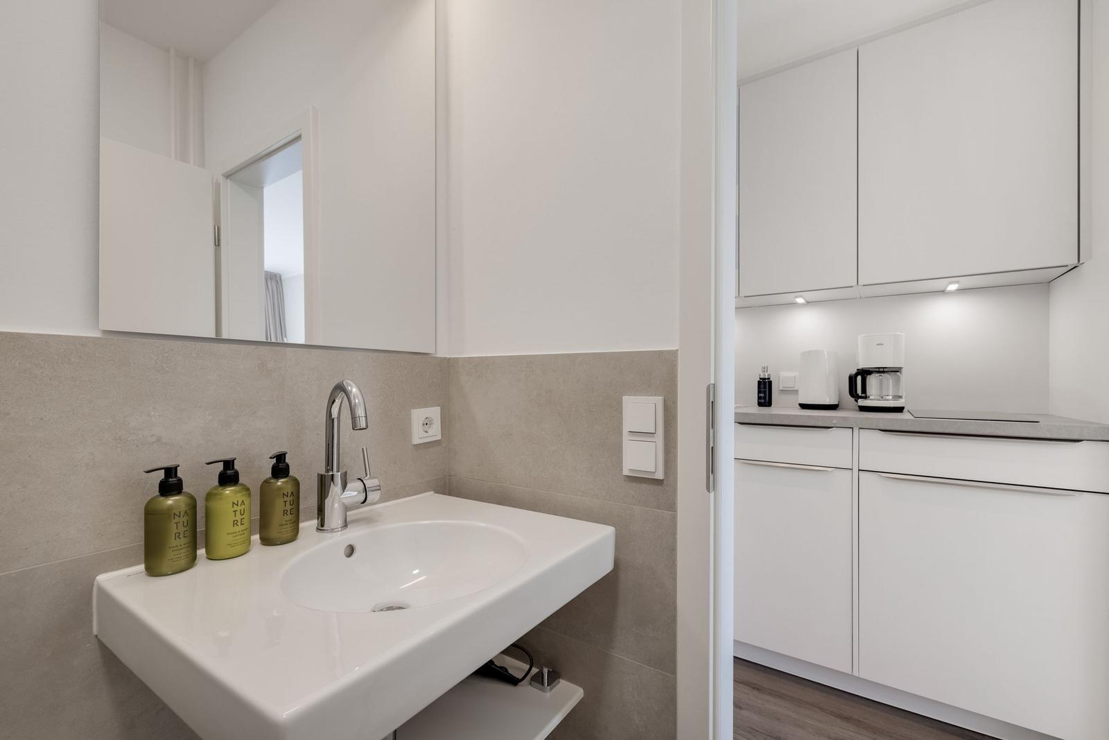 Sink with mirror and three green bottles. Kitchen with white cabinets and coffee machine.