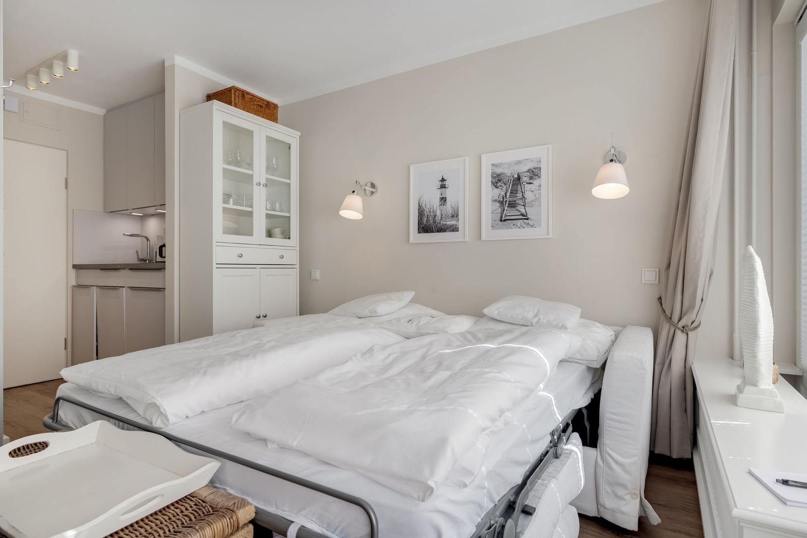 Bedroom with double bed, cabinet, and kitchen area. Wall art and lamps provide lighting.