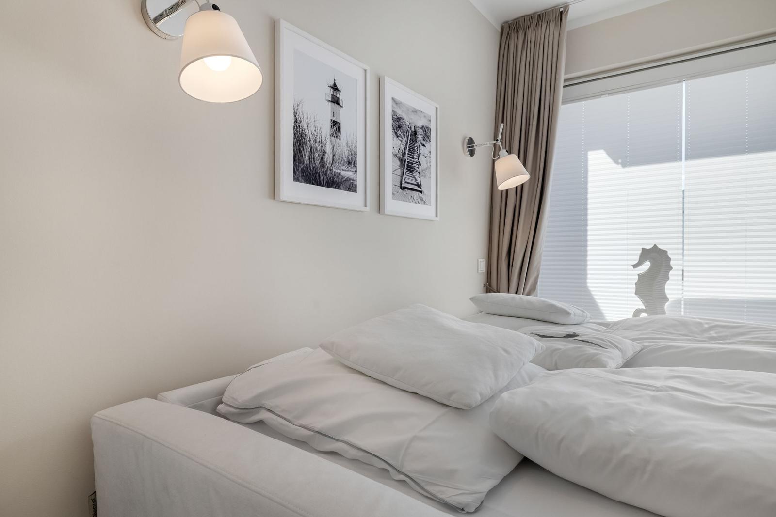 Bedroom with white bed, wall pictures, and window with blinds.