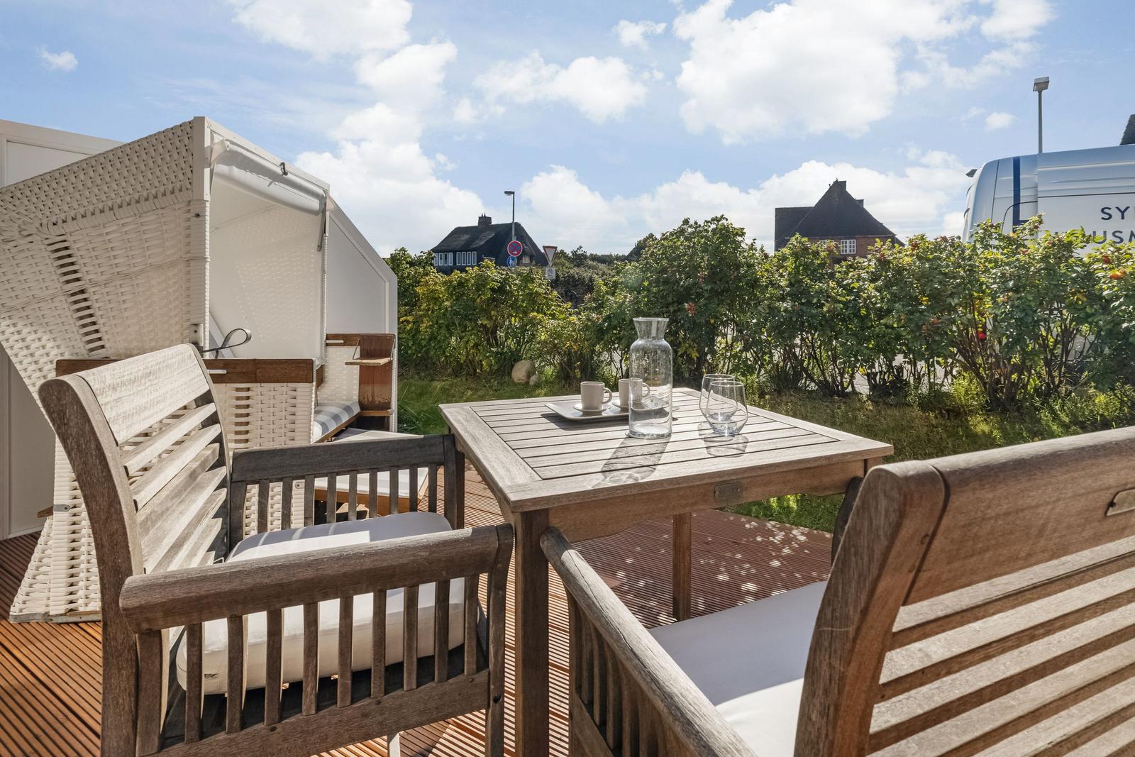 Deck with wooden table, chairs, and sunshade. View of greenery and buildings.