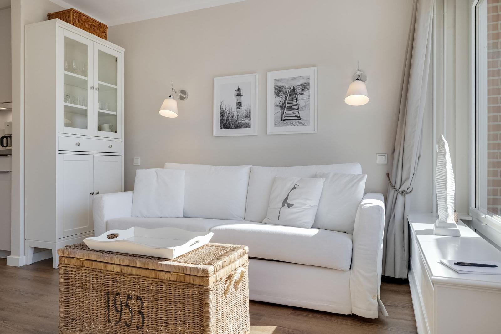 White sofa with cushions, wicker chest, and pictures on the wall.