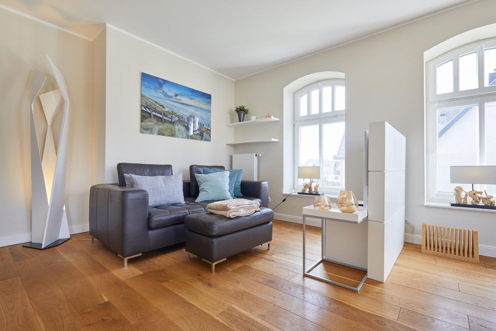 Wohnzimmer mit Sofa, Holzboden und großen Fenstern.
