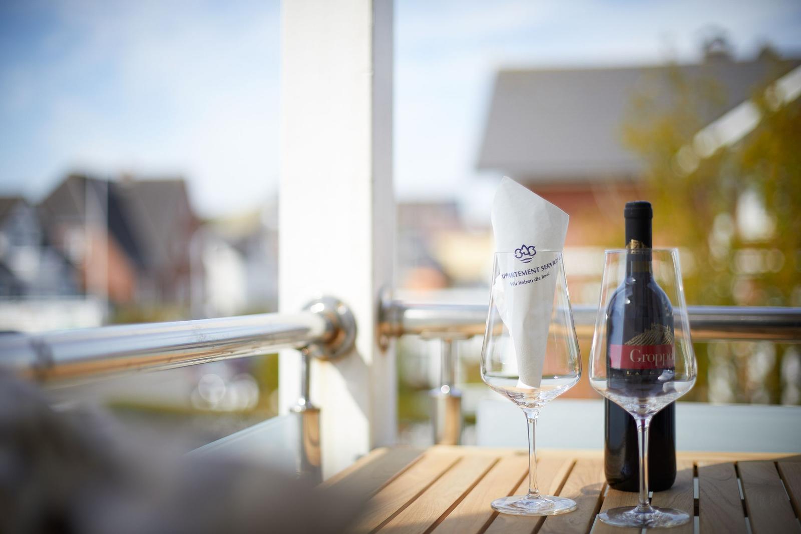 Auf der Terrasse stehen zwei Weingläser und eine Flasche Rotwein.