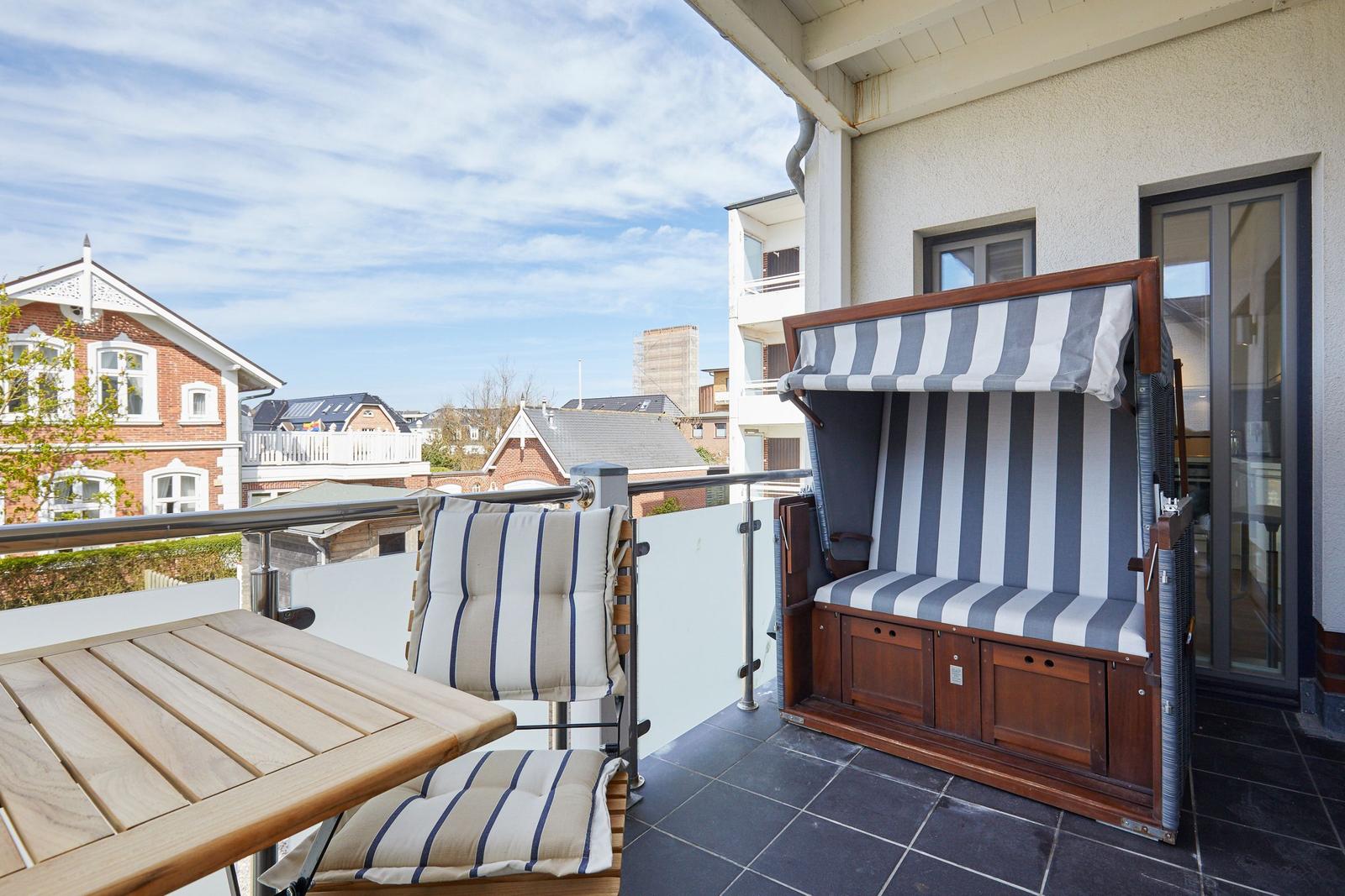 Terrasse mit Liege, Tisch und Stühlen. Blick auf Wohnhäuser und Himmel.