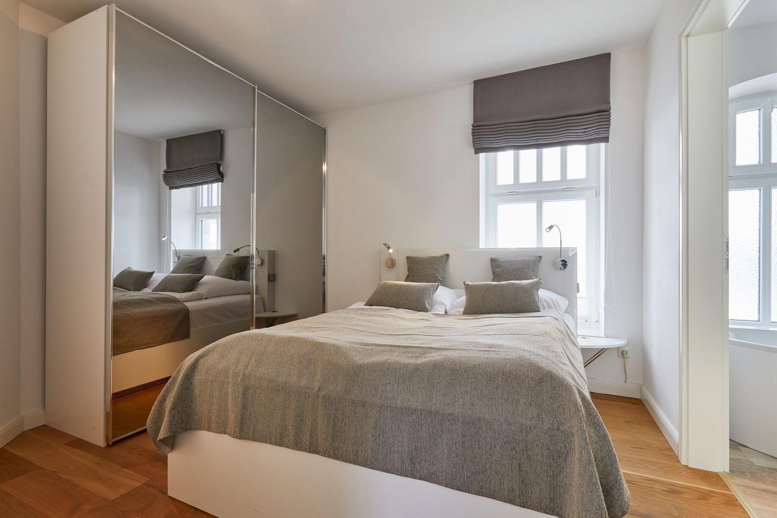 Schlafzimmer mit Bett, Spiegelschrank und Fenster mit Rollladen.