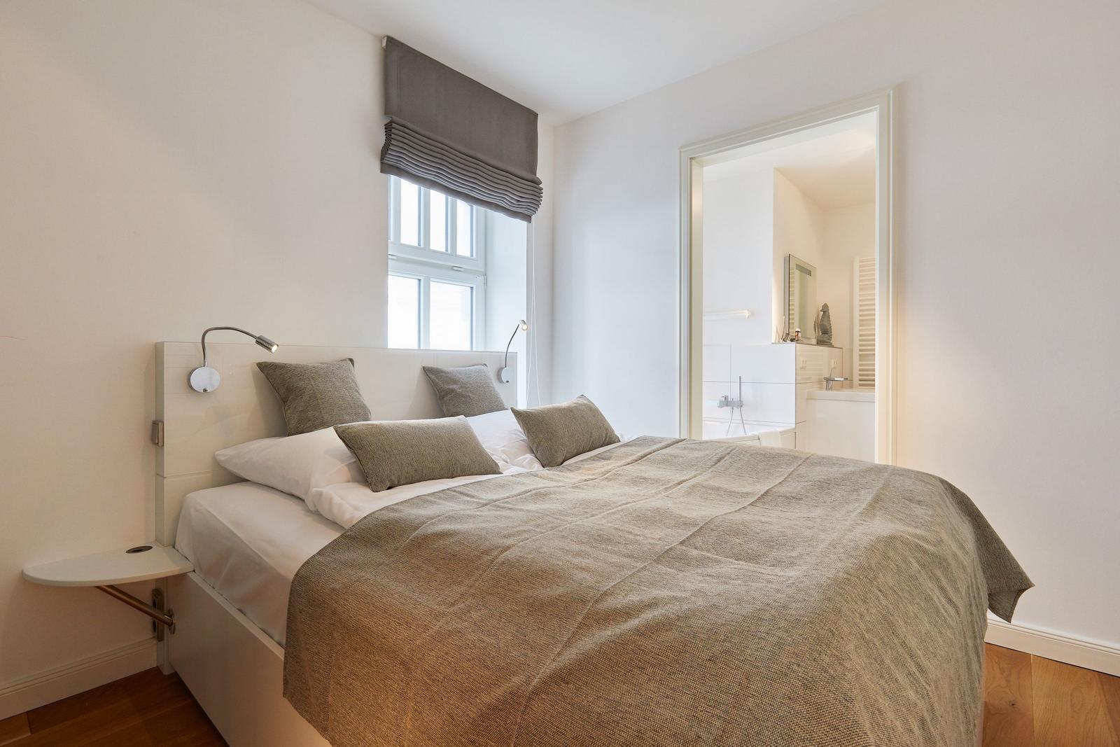 Schlafzimmer mit Bett, Fenster und angrenzender Badewanne.