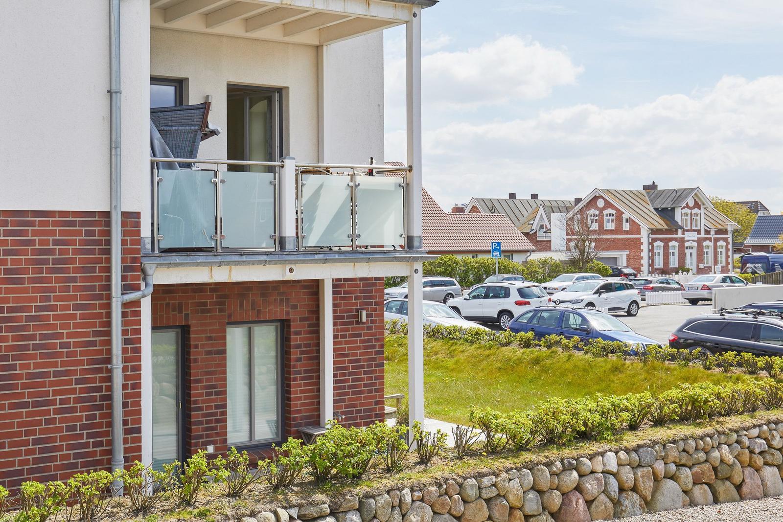Terrasse mit Glasgeländer und Blick auf Parkplatz und Häuser.