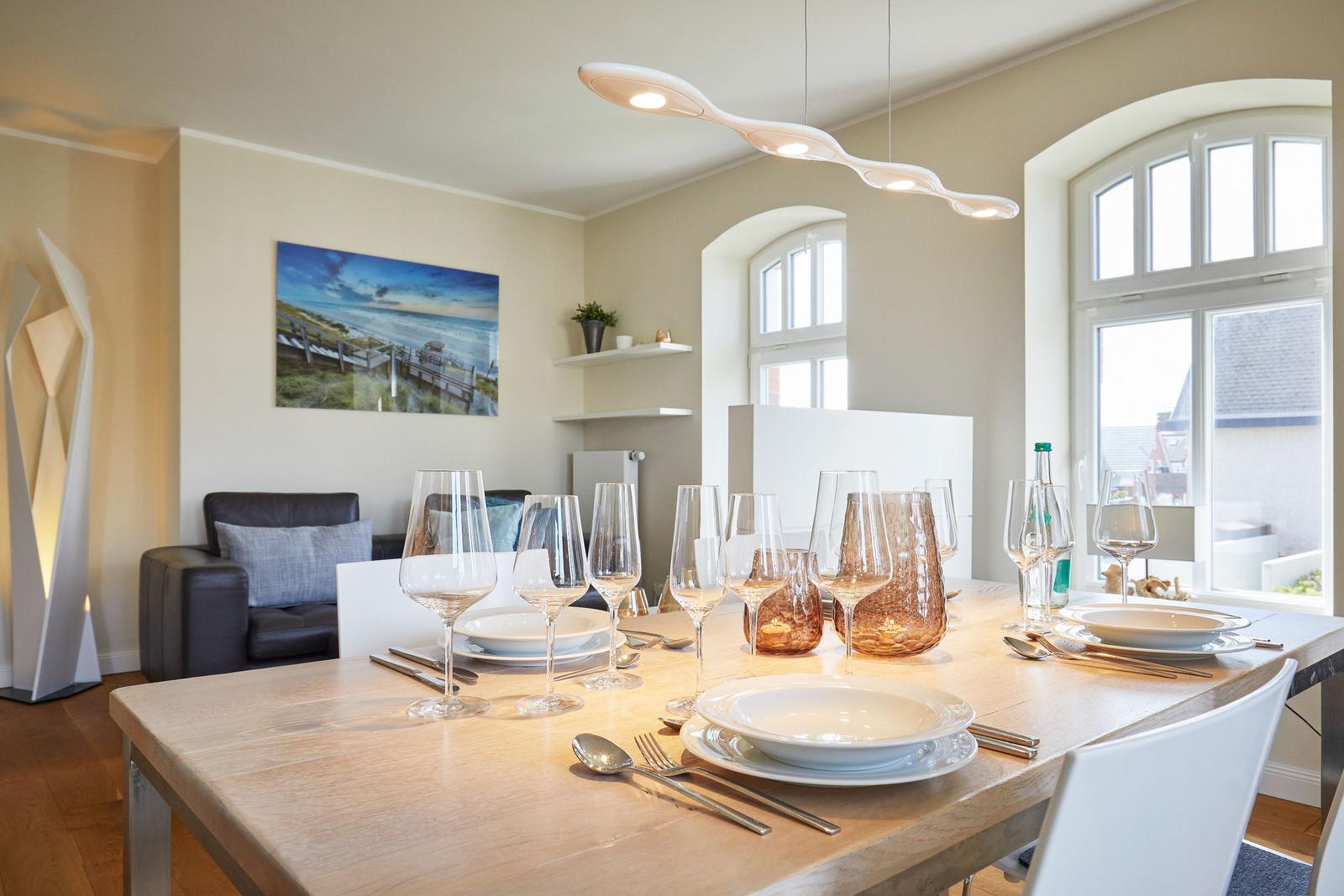 Esszimmer mit Holztisch, Gläsern und Fenstern. Wandbild und moderne Beleuchtung.