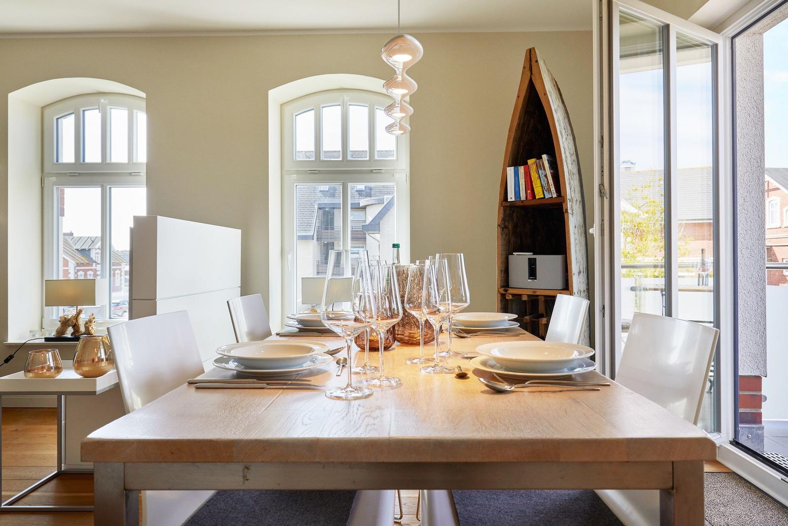 Esszimmer mit Holztisch, weißen Stühlen und Fenstern. Hintergrund: Boot als Regal.