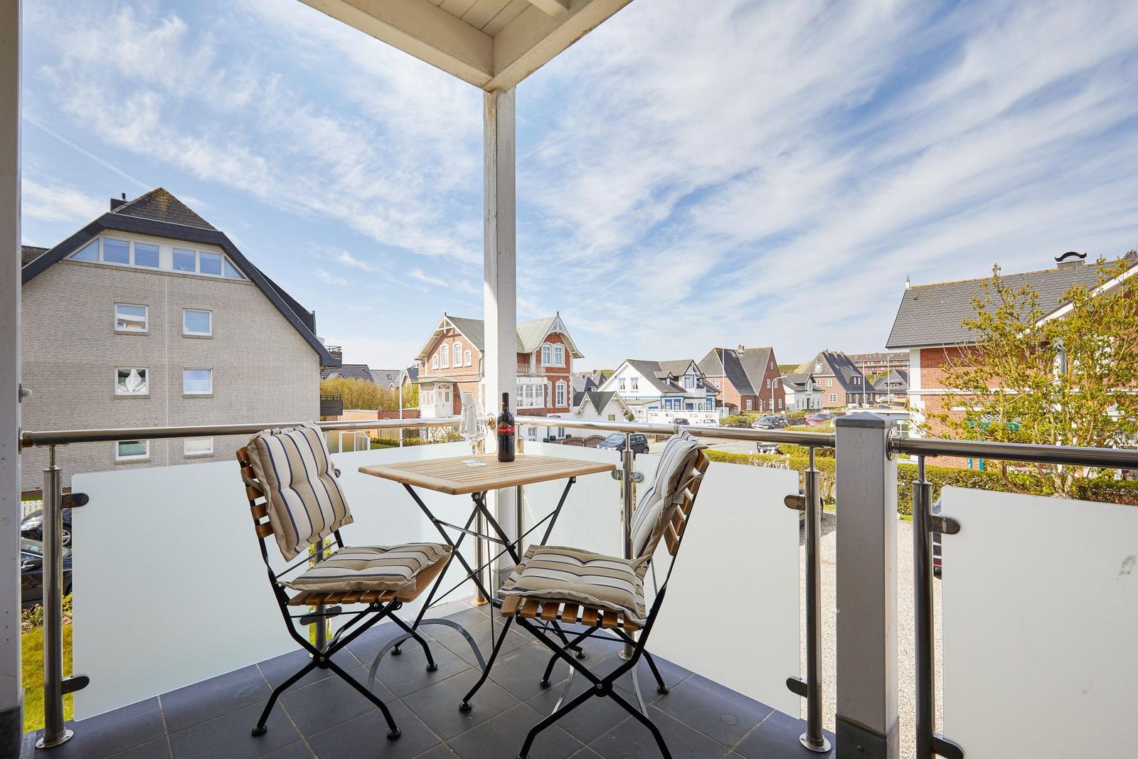 Terrasse mit Tisch und zwei Stühlen, Blick auf Wohnhäuser und Straße.