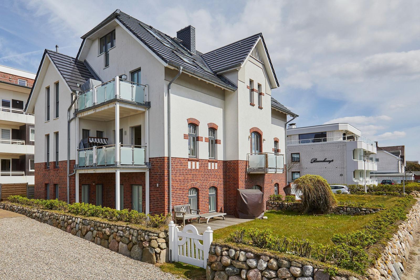 Modernes Haus mit Balkonen und Steinmauer. Grünflächen und weiße Tore.