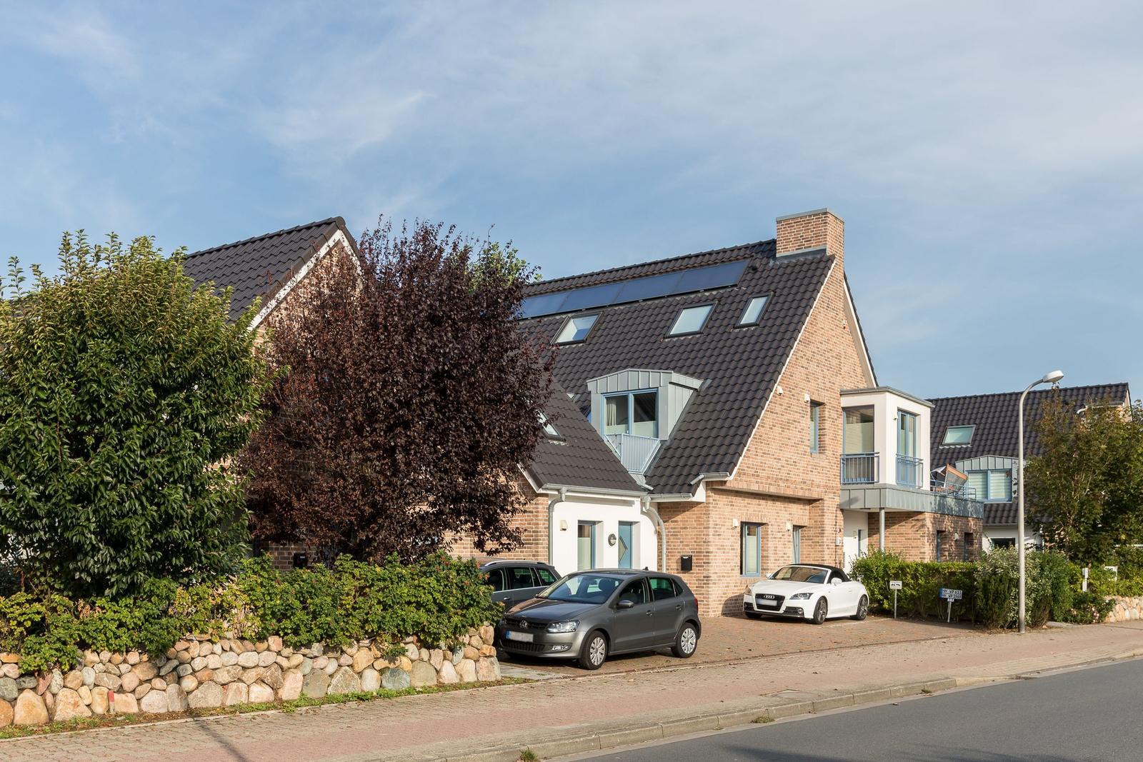 Modernes Haus mit Solaranlage und Balkonen. Zwei Autos parken vor dem Eingang.