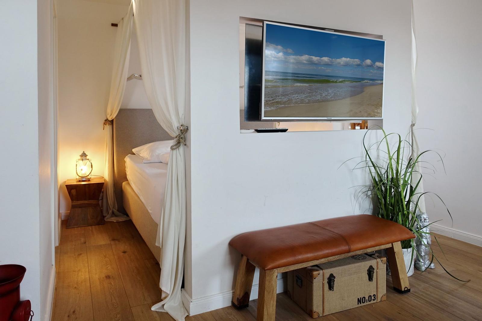 Schlafzimmer mit Bett, Fernseher und Pflanze.