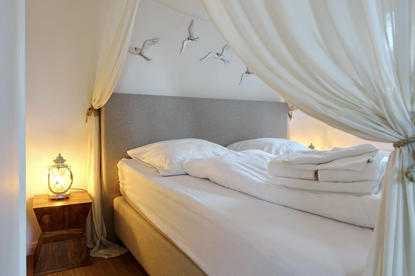 Himmelbett mit weißen Laken, Vorhängen und Vogeldekoration an der Wand.