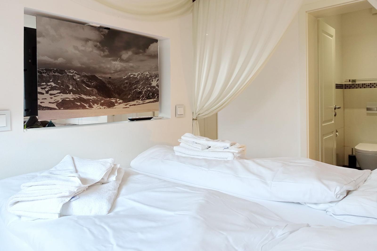 Schlafzimmer mit Bett, Handtüchern und Wandbild von Bergen.