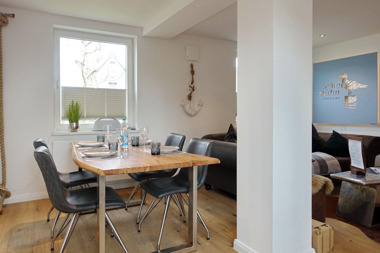 Esszimmer mit Holztisch, Stühlen und Fenster. Wohnzimmer mit Sofa und Wandbild.