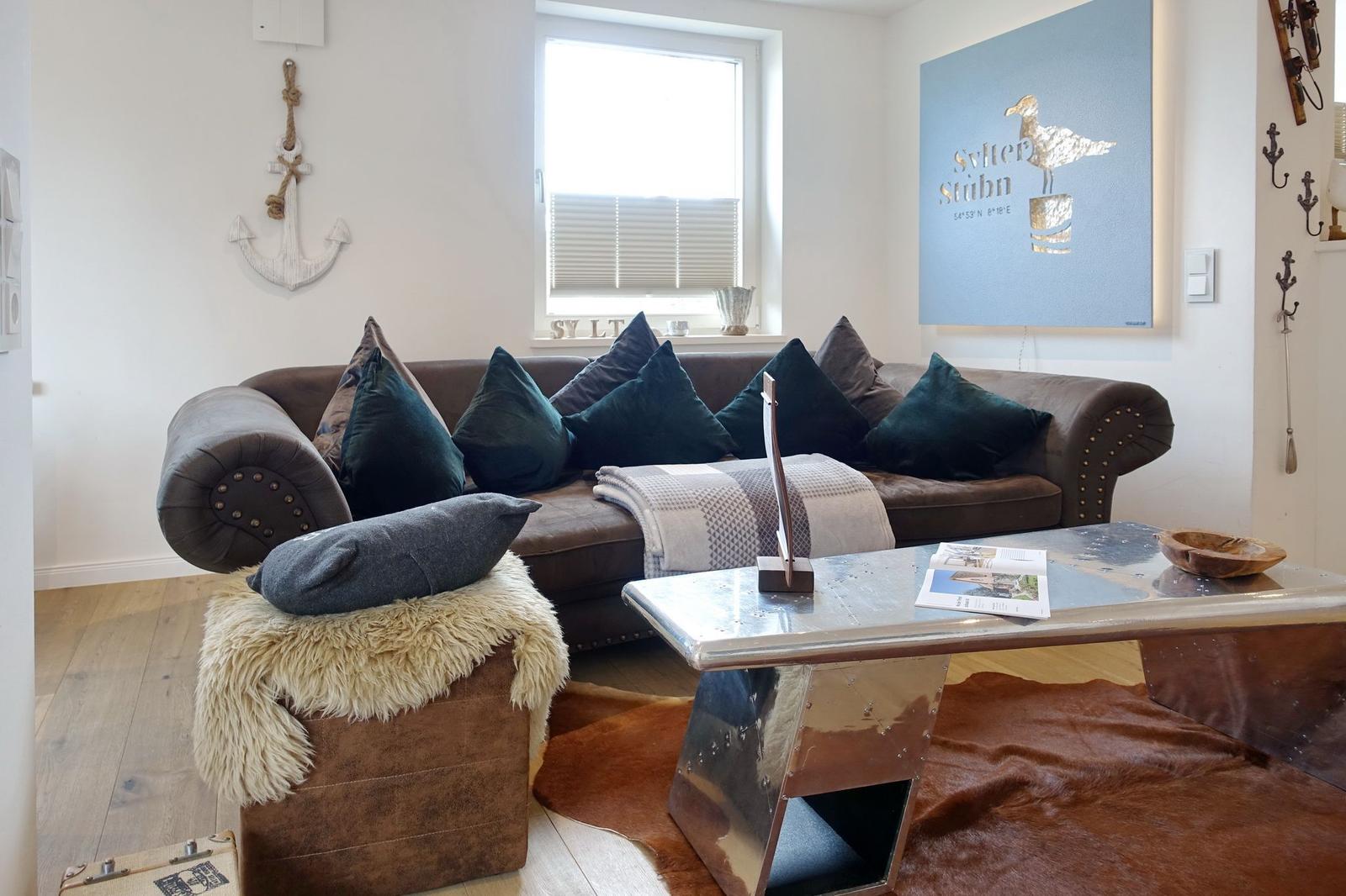 Ein Wohnzimmer mit braunem Sofa, Kissen und einem metallischen Couchtisch.