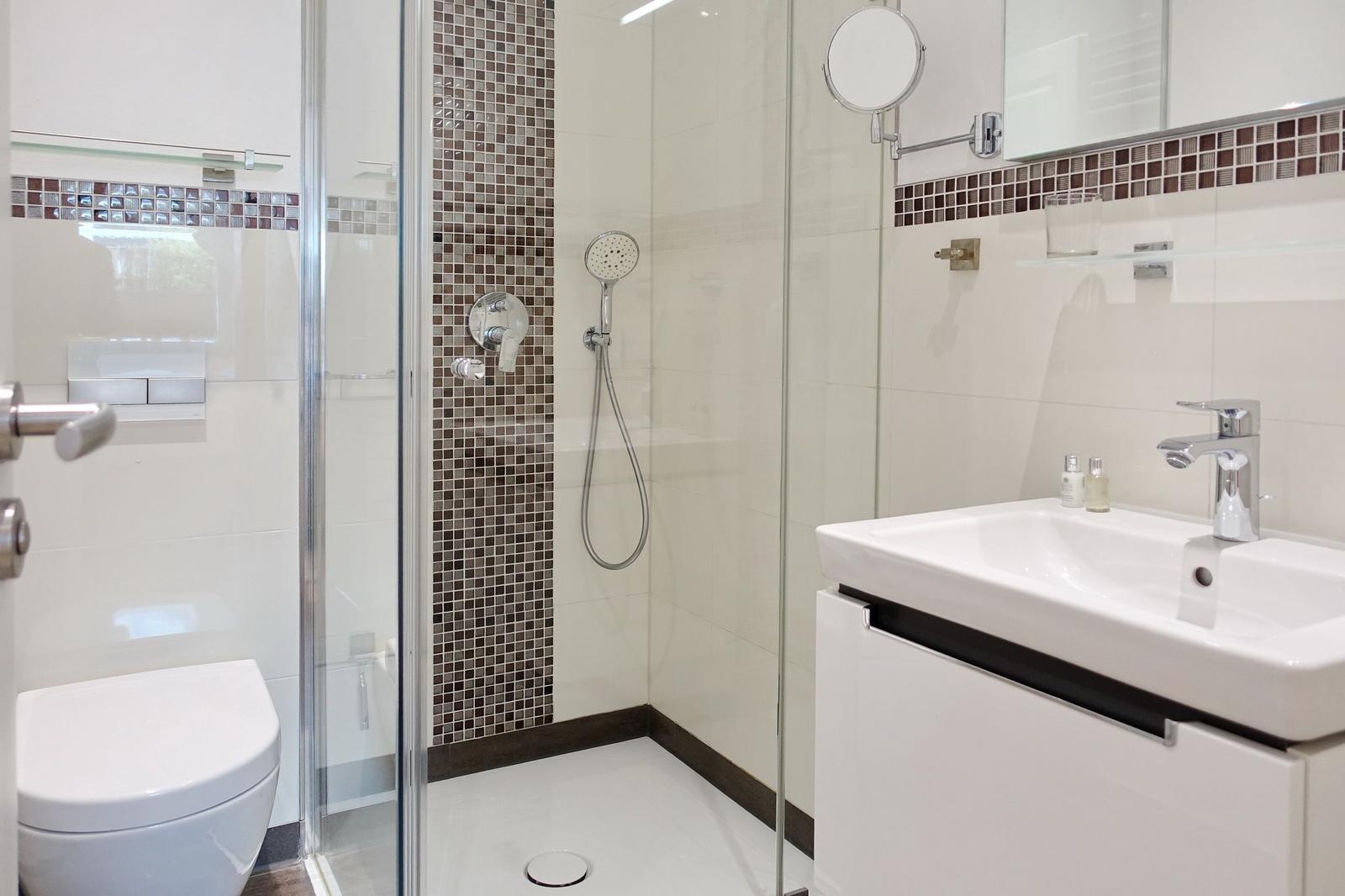 Dusche mit Glaswand, Waschbecken und Toilette in moderner Einrichtung.