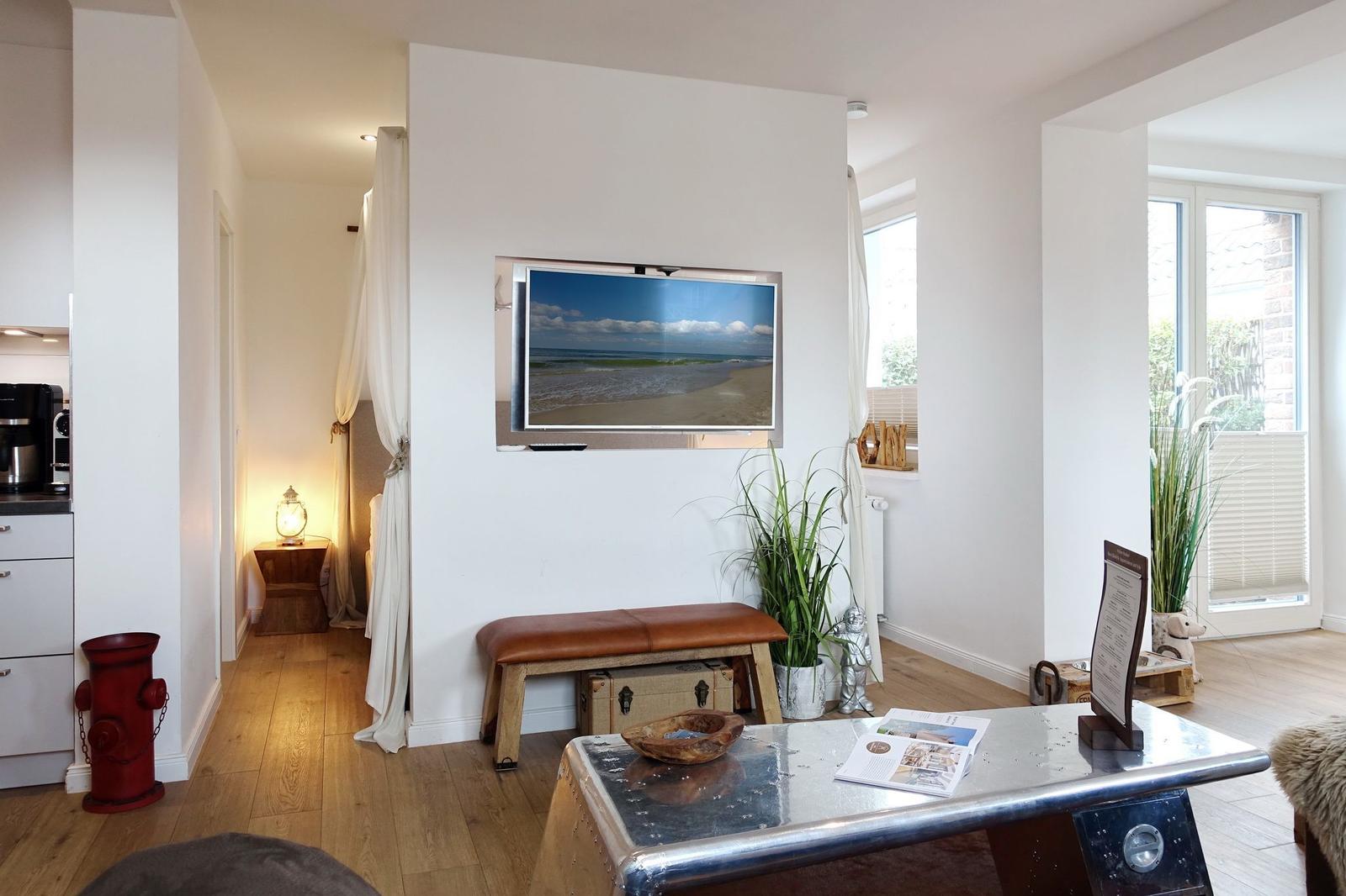 Wohnzimmer mit Fernseher, Holzboden und Pflanzen. Durchgang zur Schlafstube.
