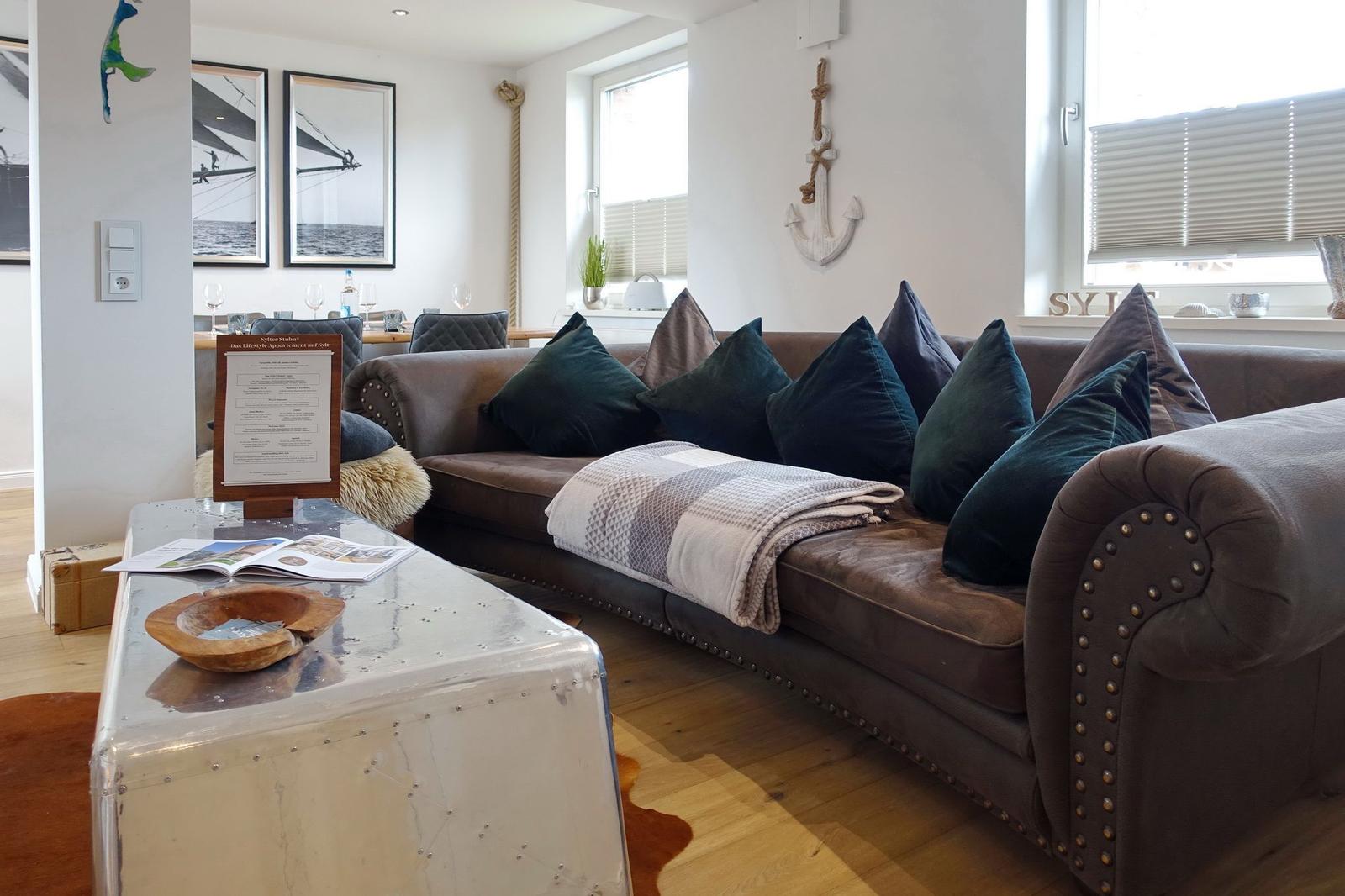 Lounge mit braunem Sofa, Kissen und Tisch. Wanddekoration mit Anker und Bildern.