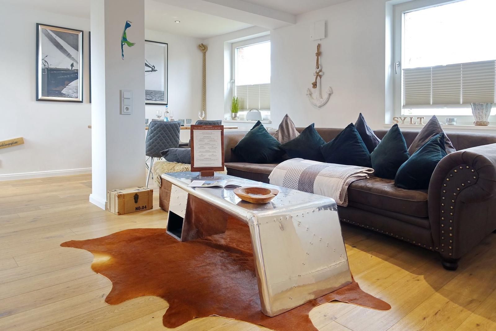 Wohnzimmer mit braunem Sofa, Metalltisch und Lederhaut auf Holzboden.