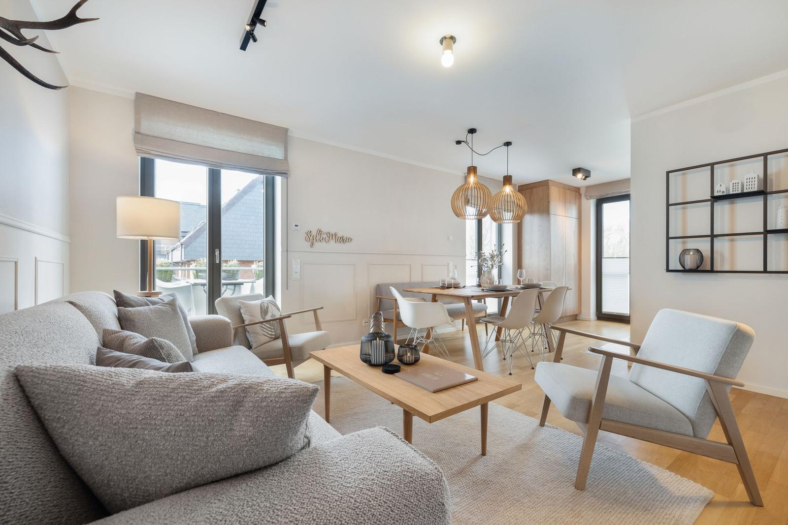 Living and dining area with sofa, chairs, and table. Wooden and metal furniture. Windows and ceiling lights.