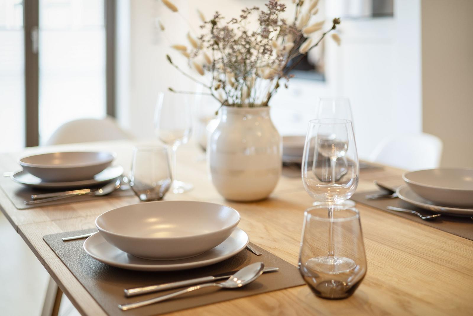 Dining table with dishes, glasses, and vase flowers.