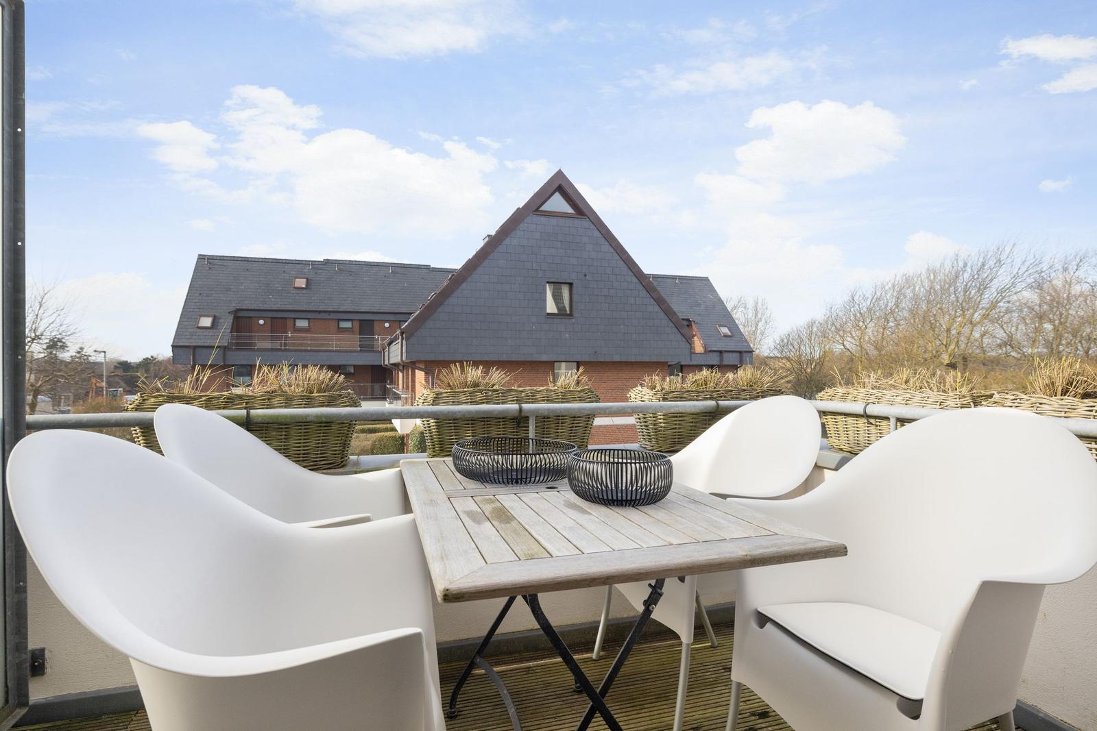 Terrace with white table and chairs, view of a house with slate roof.