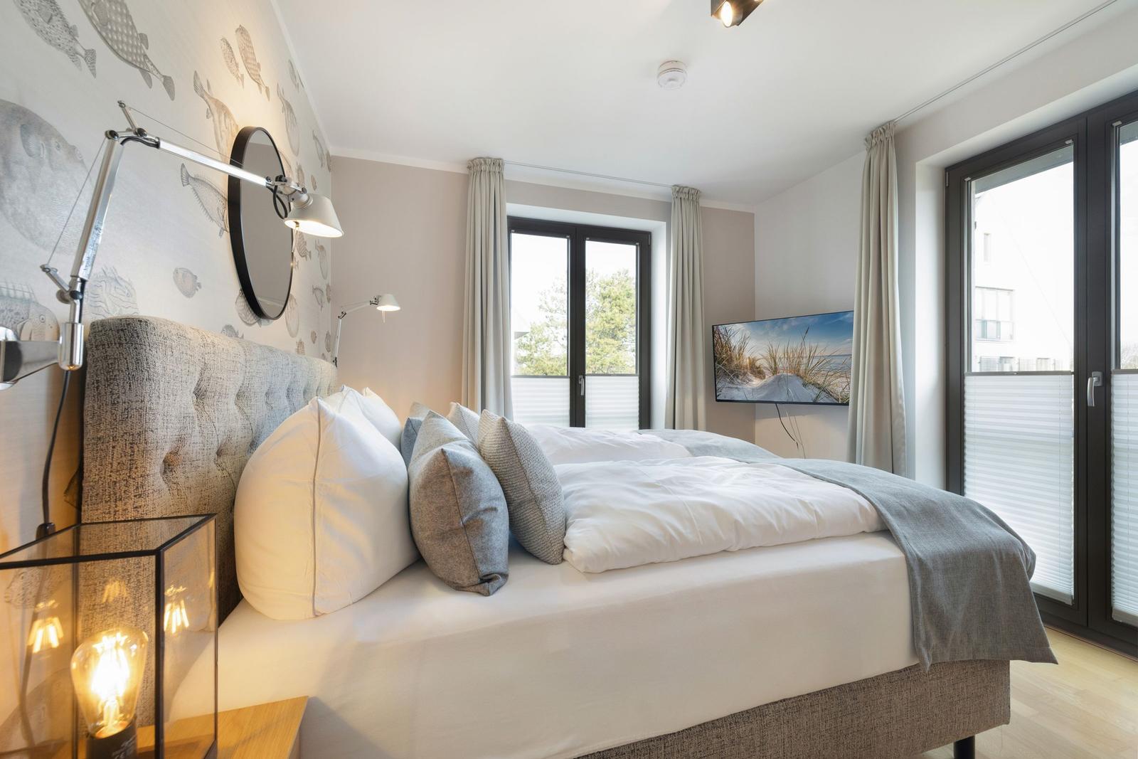 Bedroom with bed, windows, and wall art. Wall with fish motif and standing lamp.
