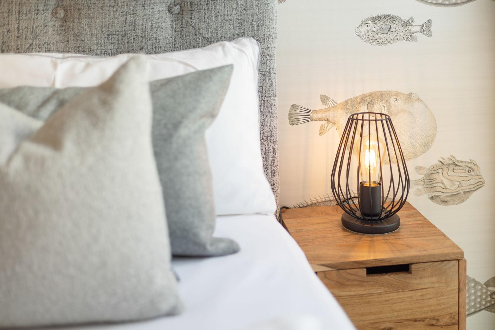 Bedroom with bed, pillows, and nightstand with lamp. Wall with fish motifs.