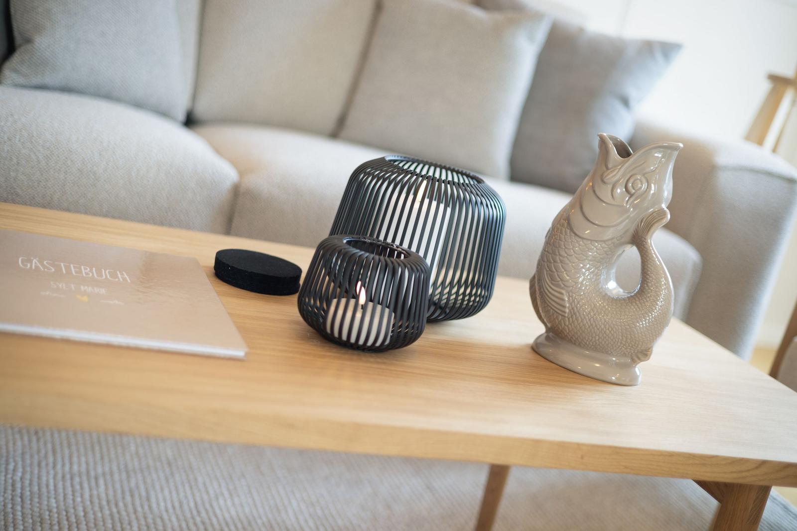 Wooden table with fish figurine, candle holders, and guest book in front of a sofa.