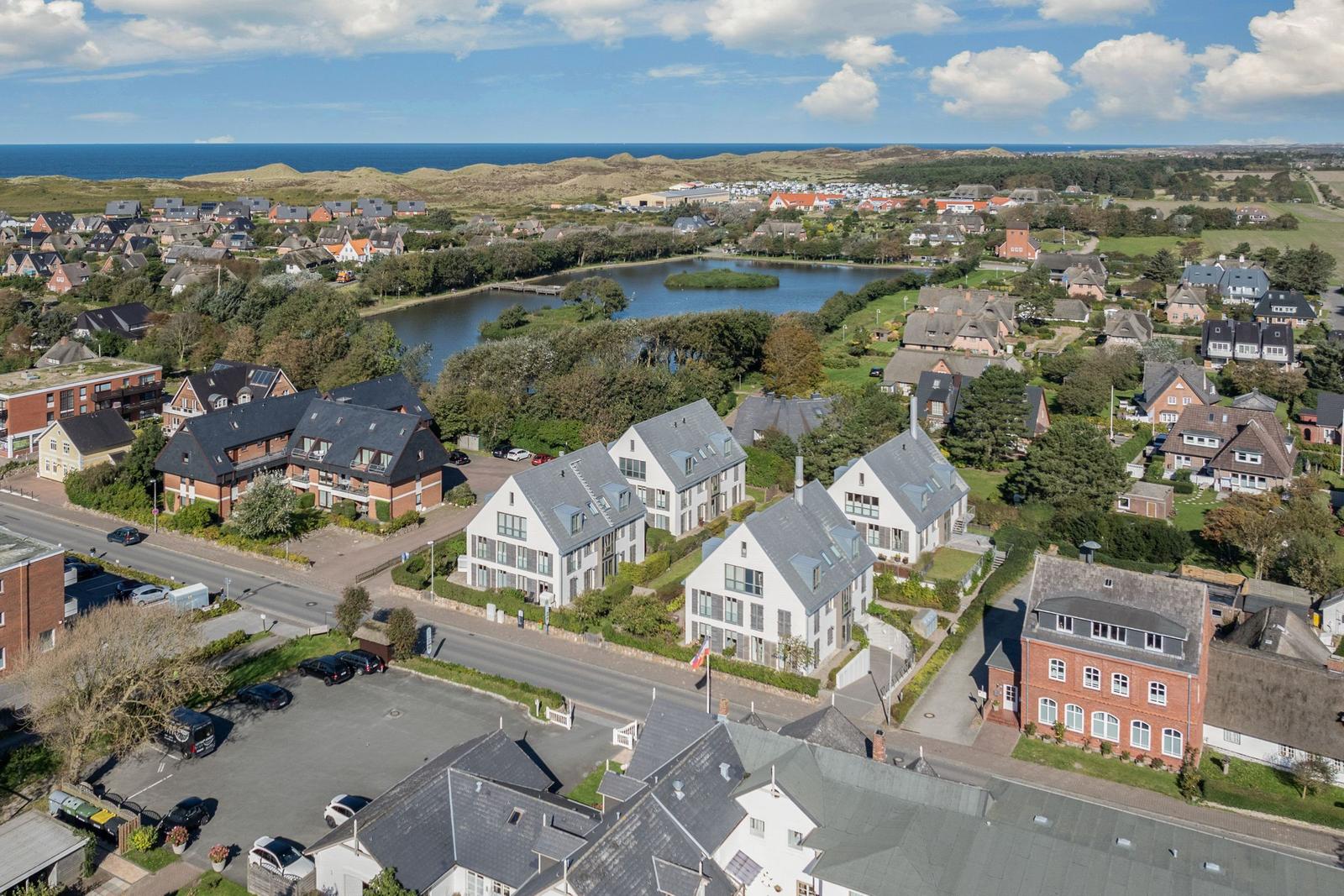 Aerial view of a coastal village with houses, a lake, and the sea in the background.