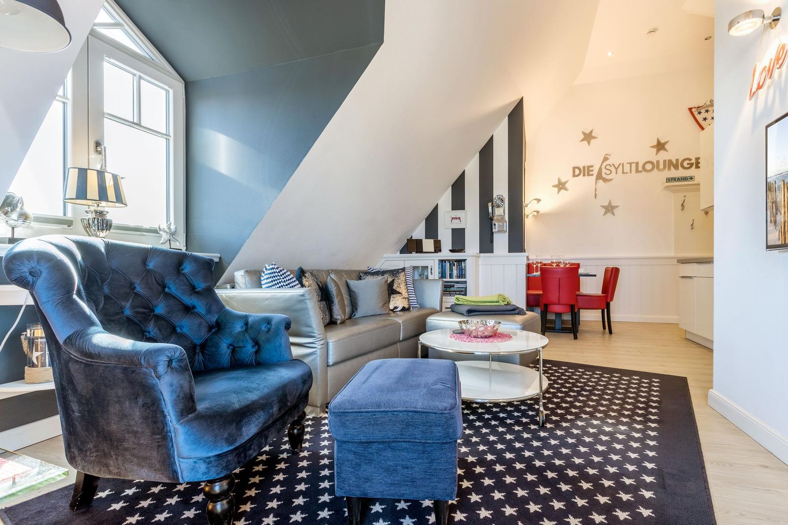 Living area with blue upholstered chair, sofa, and star-patterned rug under sloped ceiling.