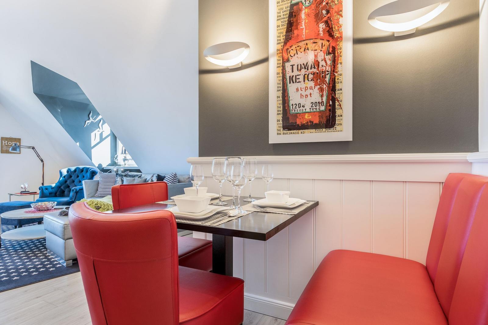 Dining table with red chairs and wall art on gray wall.