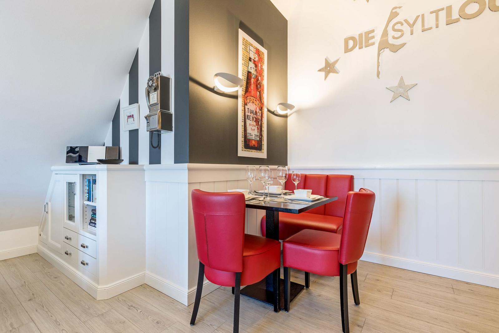 Dining area with red chairs and table, wall decor and cabinet
