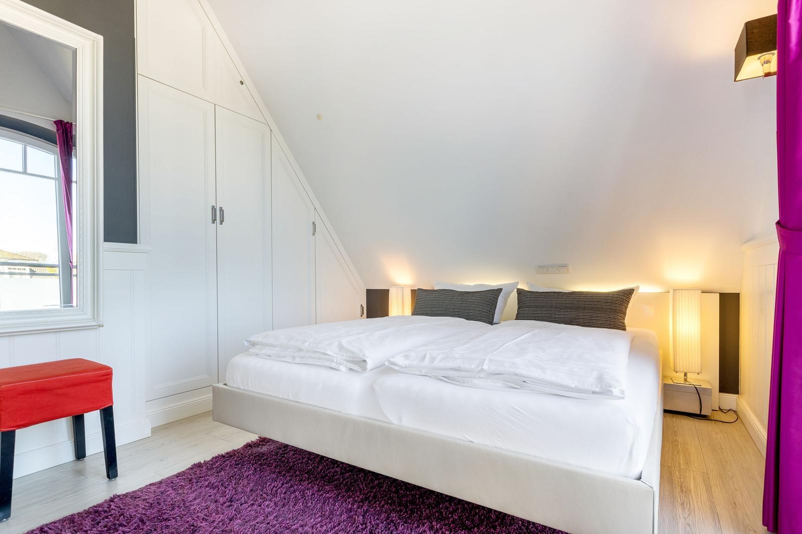 Bedroom with double bed, white wardrobes, and purple rug.