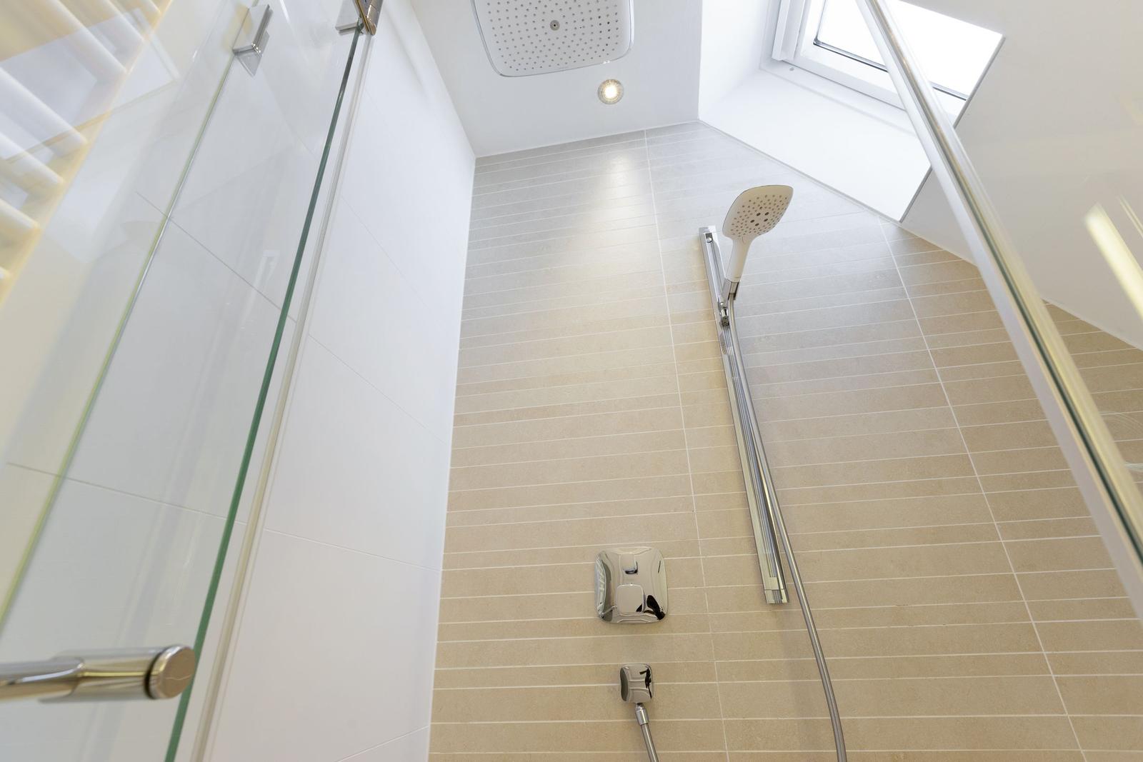 Shower with glass enclosure, showerhead, and handheld shower on floor tiles.
